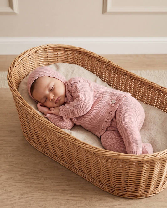 Baby sleeping in Moses basket wearing traditional Spanish dusty pink knitted take-me-home set with matching bonnet.