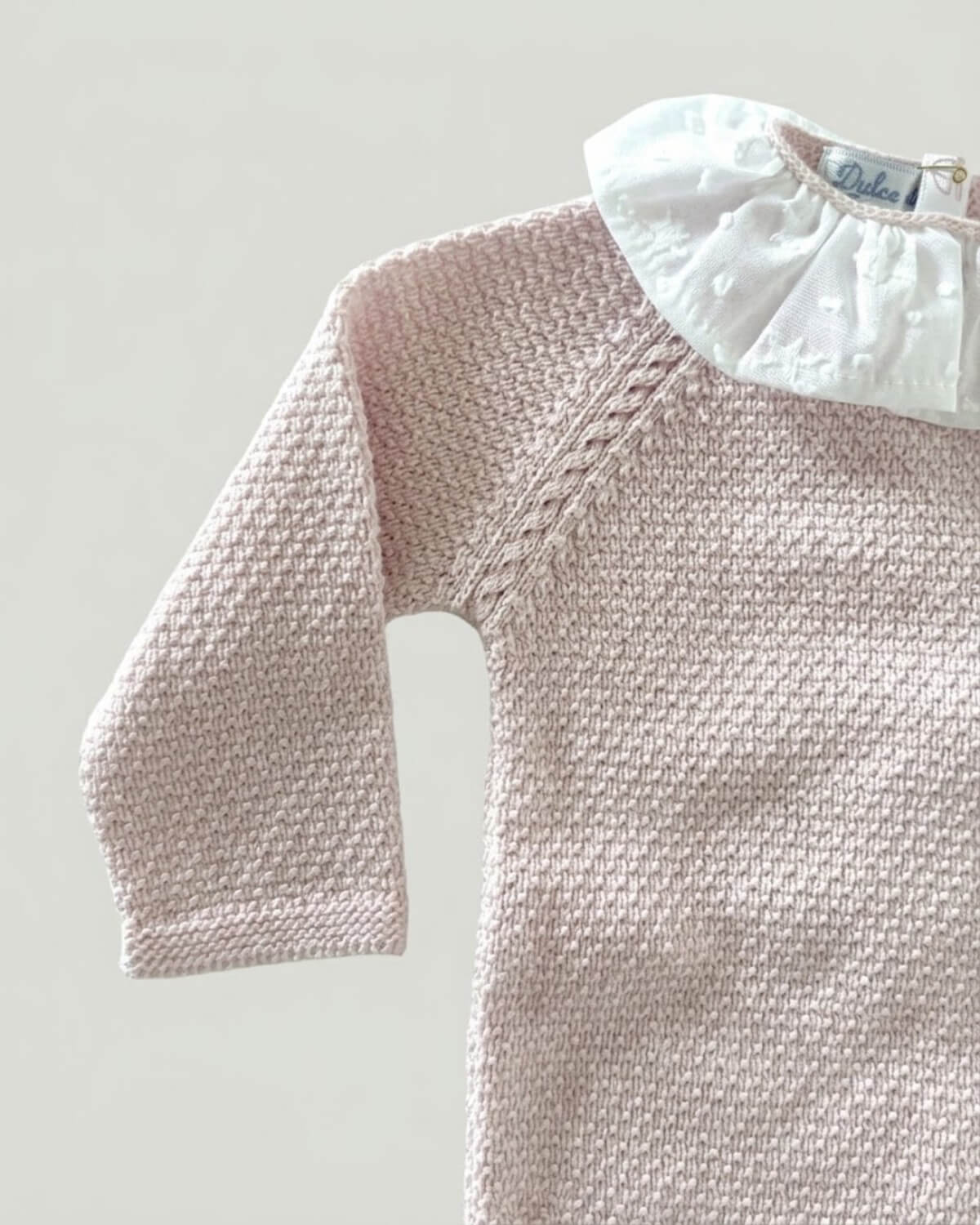 Folded pale pink knitted baby jumper with white embroidered star frill collar.