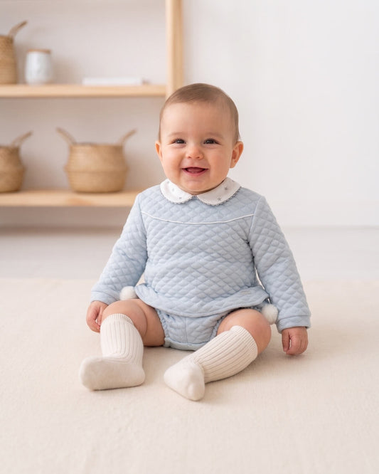 Baby boy wearing traditional Spanish blue quilted two-piece set with embroidered star collar and cream knee socks.