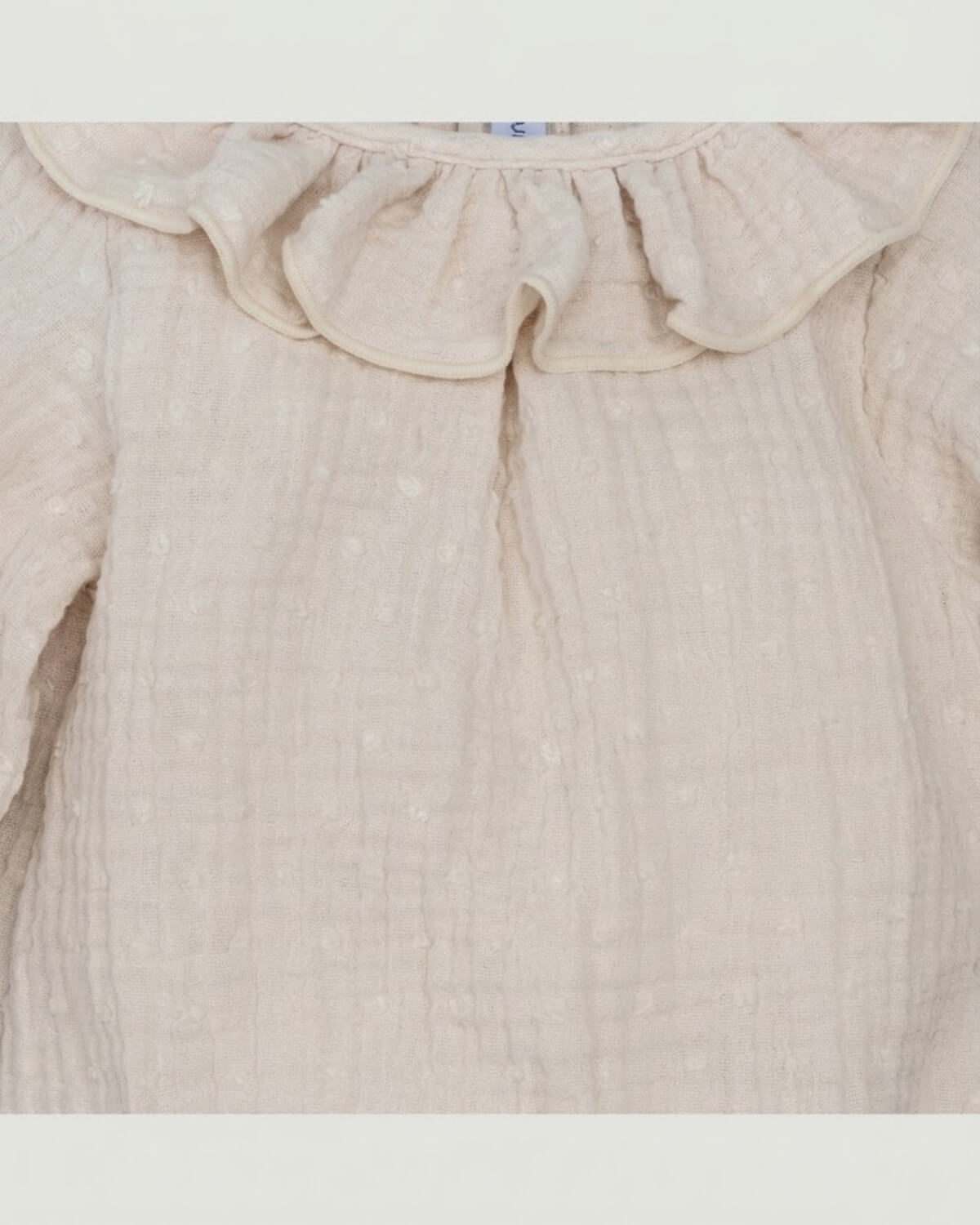 Close-up detail of frilled ruffle collar and textured plumeti double gauze cotton on cream Spanish baby romper.