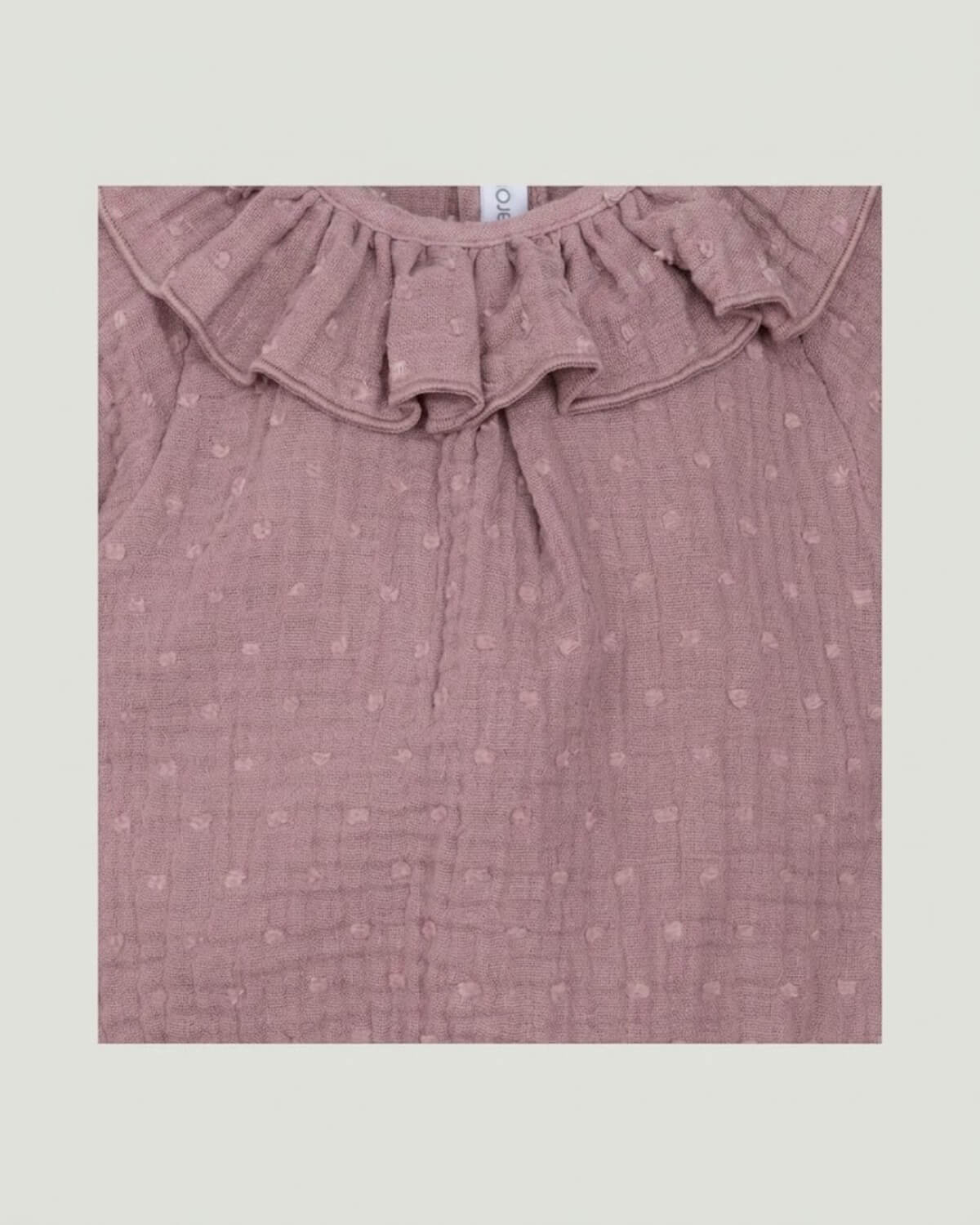 Close-up detail of frilled ruffle collar and textured plumeti double gauze cotton on dusty pink Spanish baby romper.