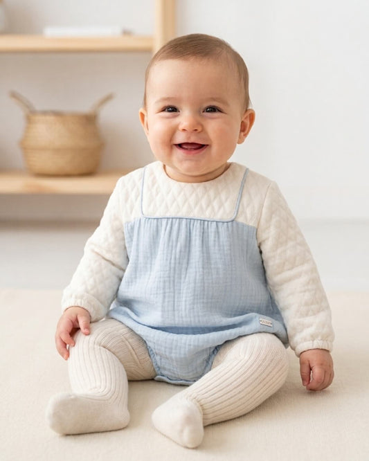 Baby wearing traditional Spanish baby romper in blue and white with ribbed tights.