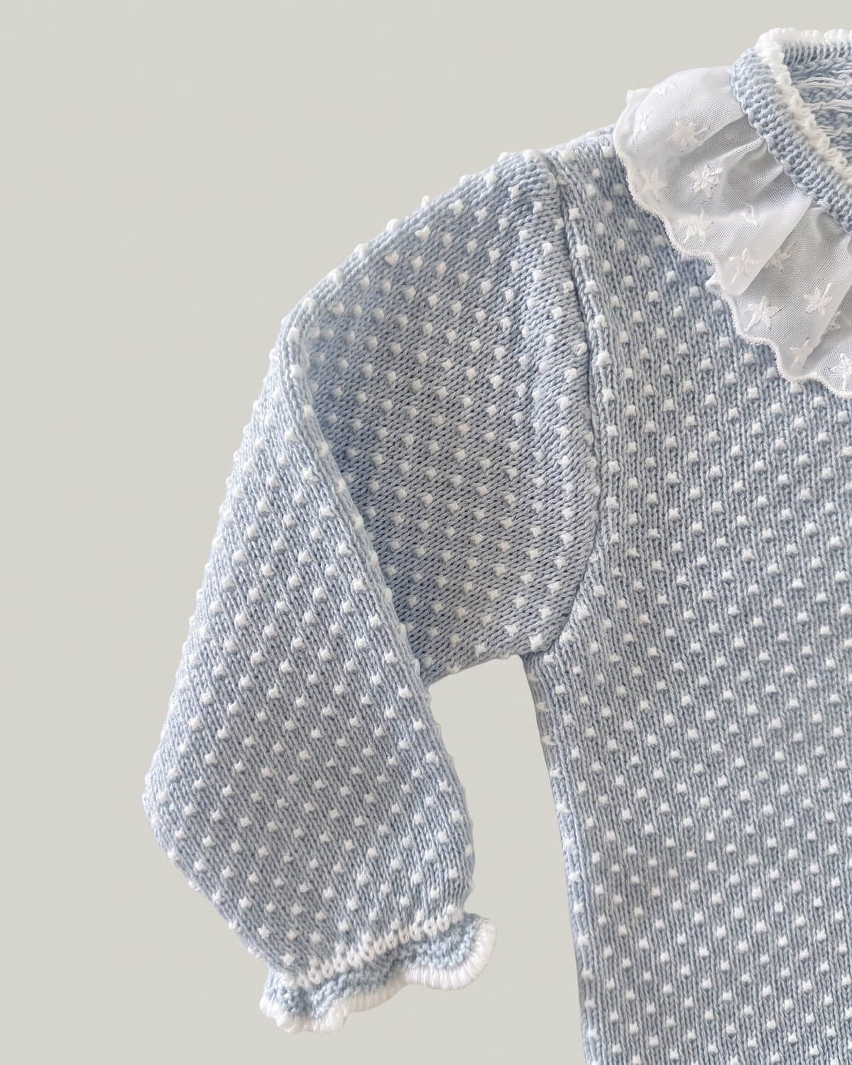 Close-up detail of organza frill collar and polka dot knit texture on light blue Spanish baby jumper.