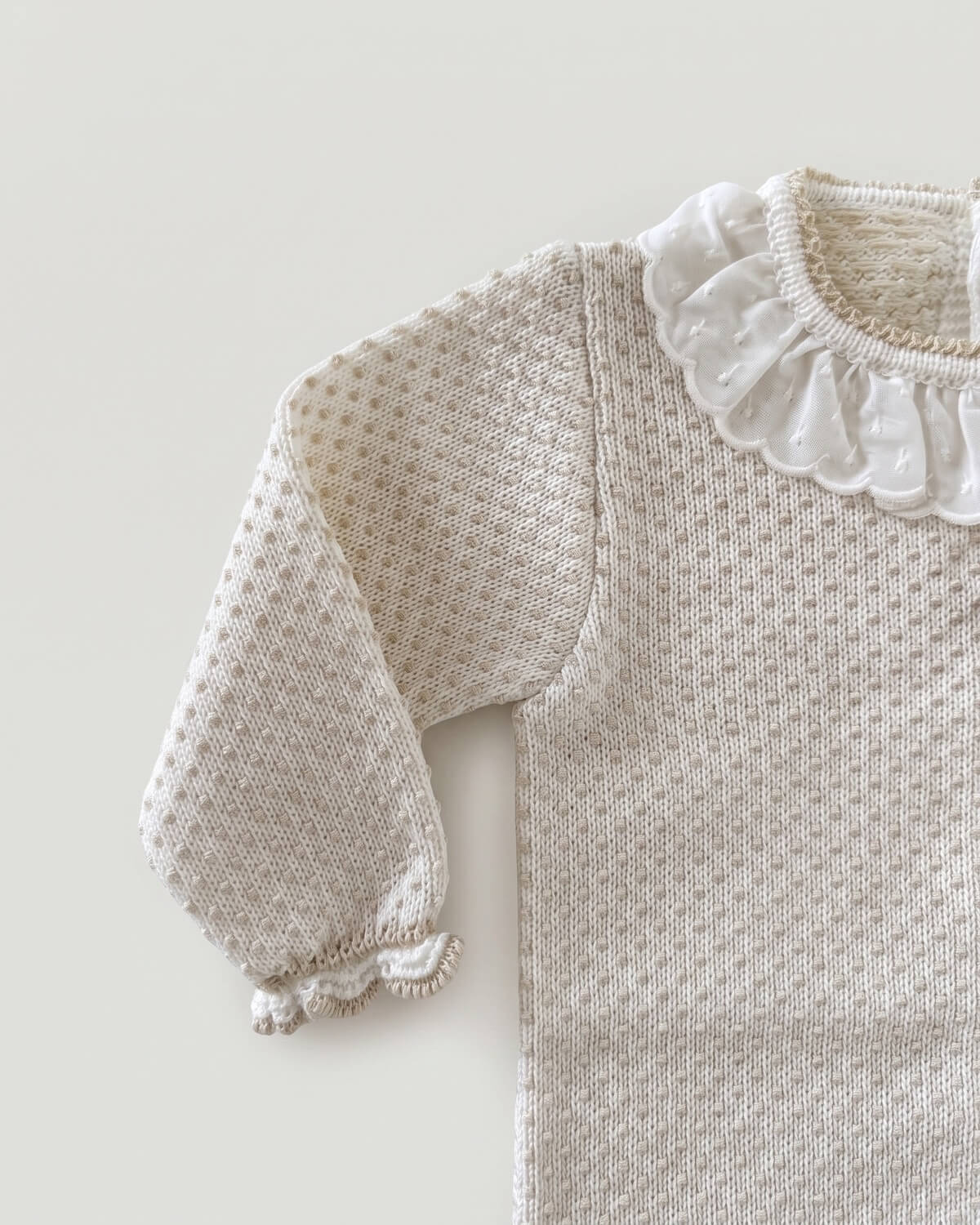 Close-up detail of frilled lace collar and textured knit on beige Spanish baby jumper