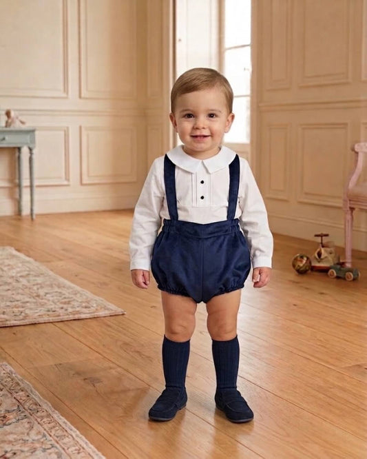 Baby boy wearing traditional Spanish white shirt and navy velvet braces bloomers with matching navy knee socks.