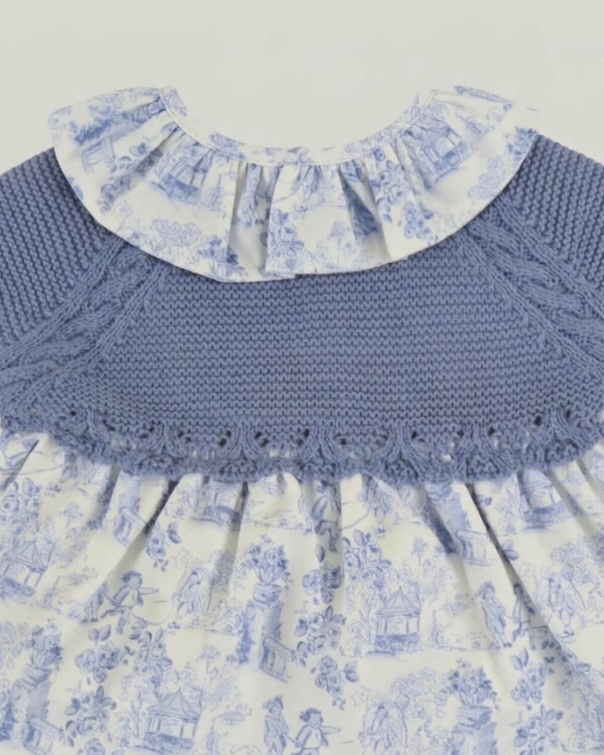 Close-up detail of dusty blue knitted yoke with scalloped hem and frilled toile de Jouy collar on Spanish baby dress.