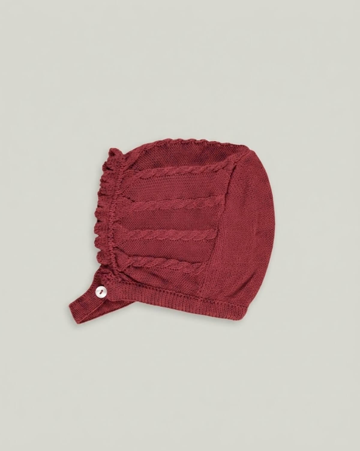 Detail view of traditional Spanish baby bonnet in burgundy cable knit with button closure.