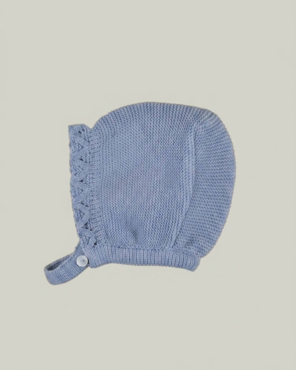 Detail view of traditional Spanish baby bonnet in dusty blue knit with eyelet pattern and button closure.