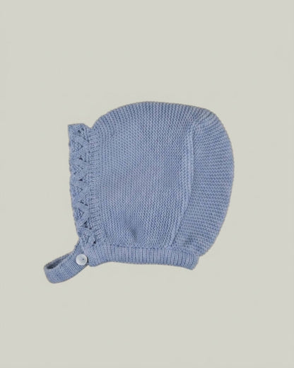 Detail view of traditional Spanish baby bonnet in dusty blue knit with eyelet pattern and button closure.