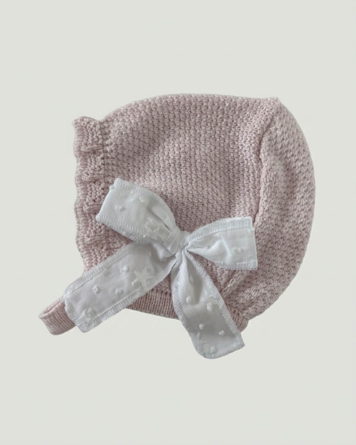Matching pale pink knitted baby bonnet featuring a white star ribbon bow detailing.L