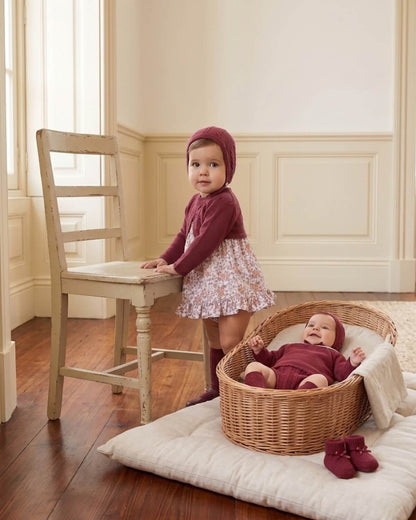 Baby siblings wearing matching Dulce de Fresa traditional Spanish burgundy knitted collection with floral print dress and cable knit set.