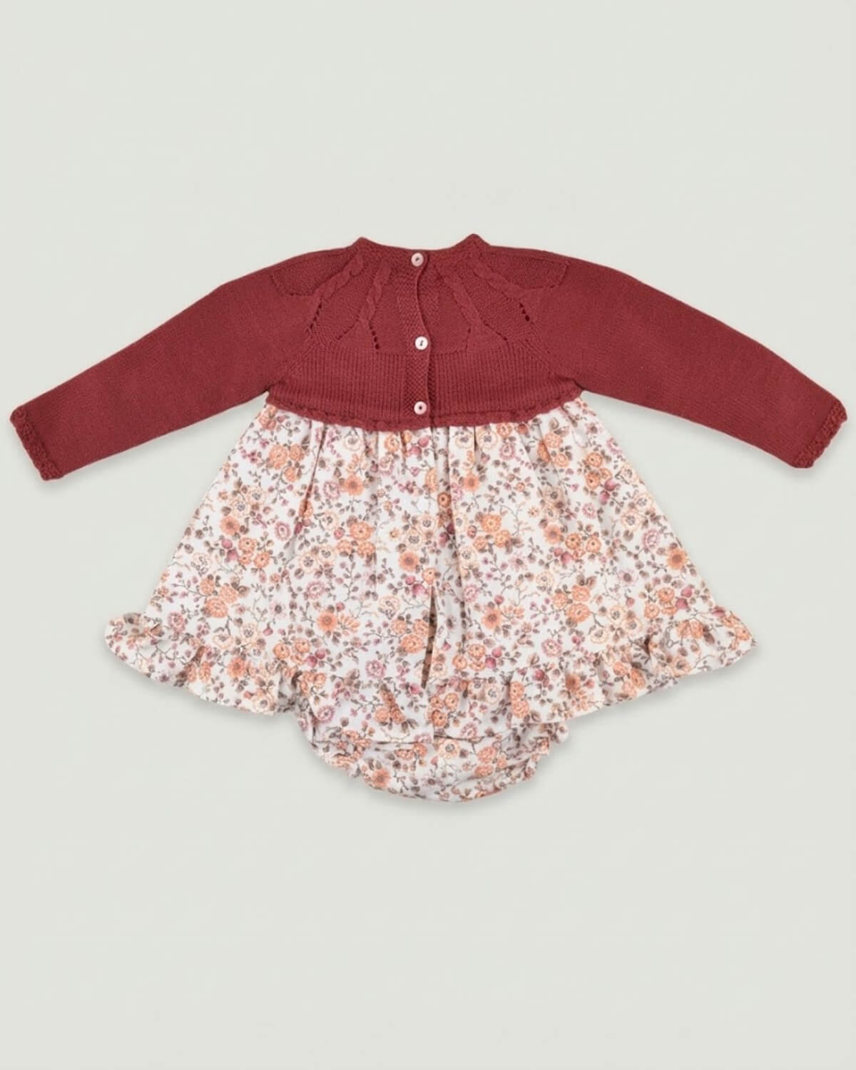 Back view of traditional Spanish baby dress showing burgundy knitted yoke with button closure and floral print skirt.
