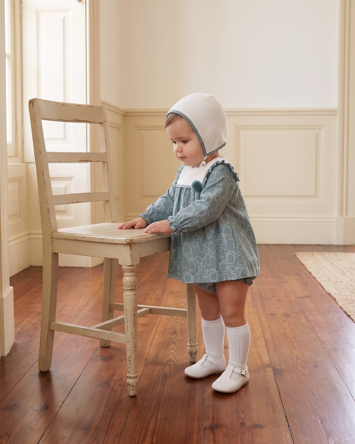 Baby girl wearing traditional Spanish printed dress set with matching bonnet, knee socks and T-bar shoes.