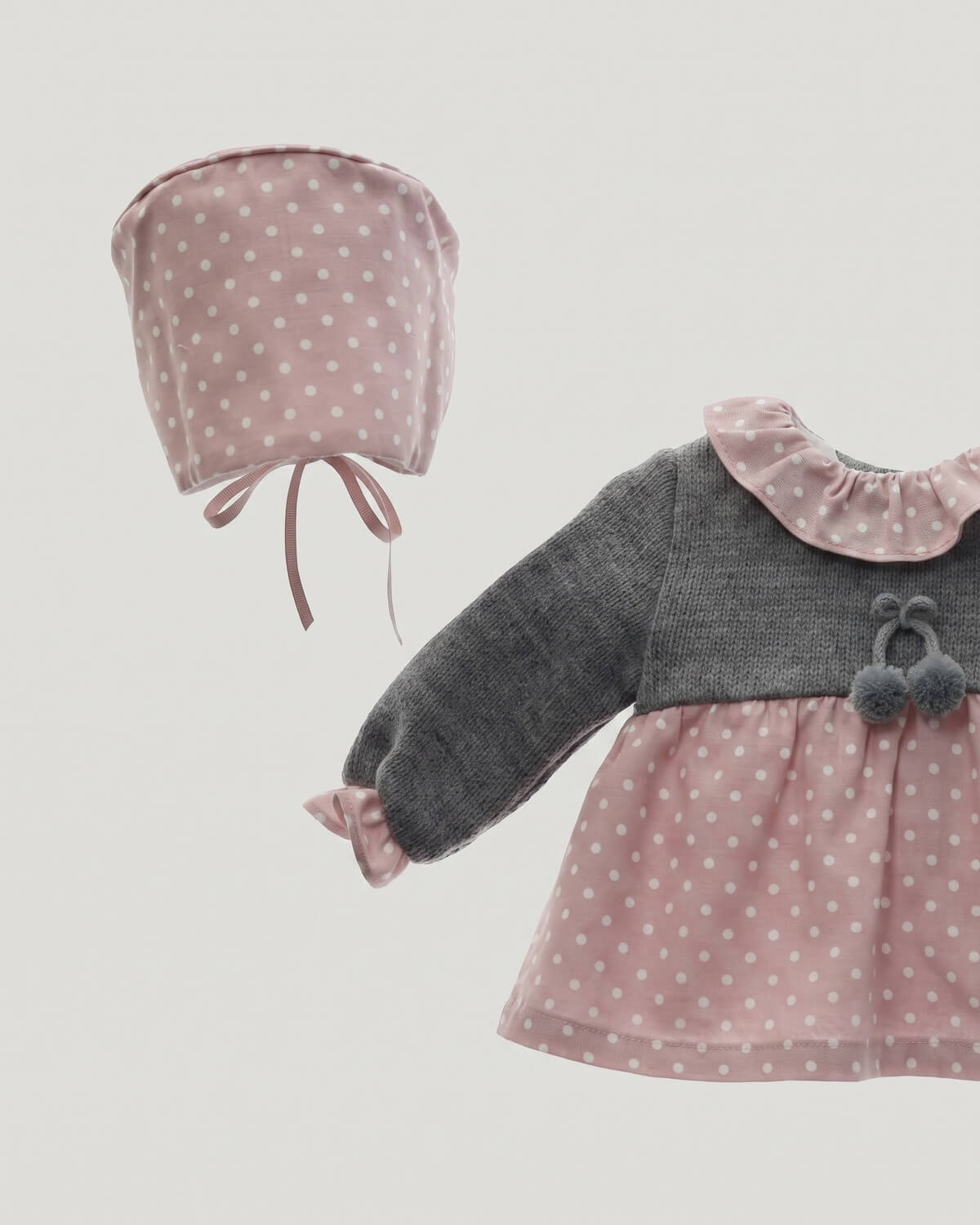 Close-up detail of grey knitted bodice with pom-poms, frilled polka dot collar and matching bonnet.