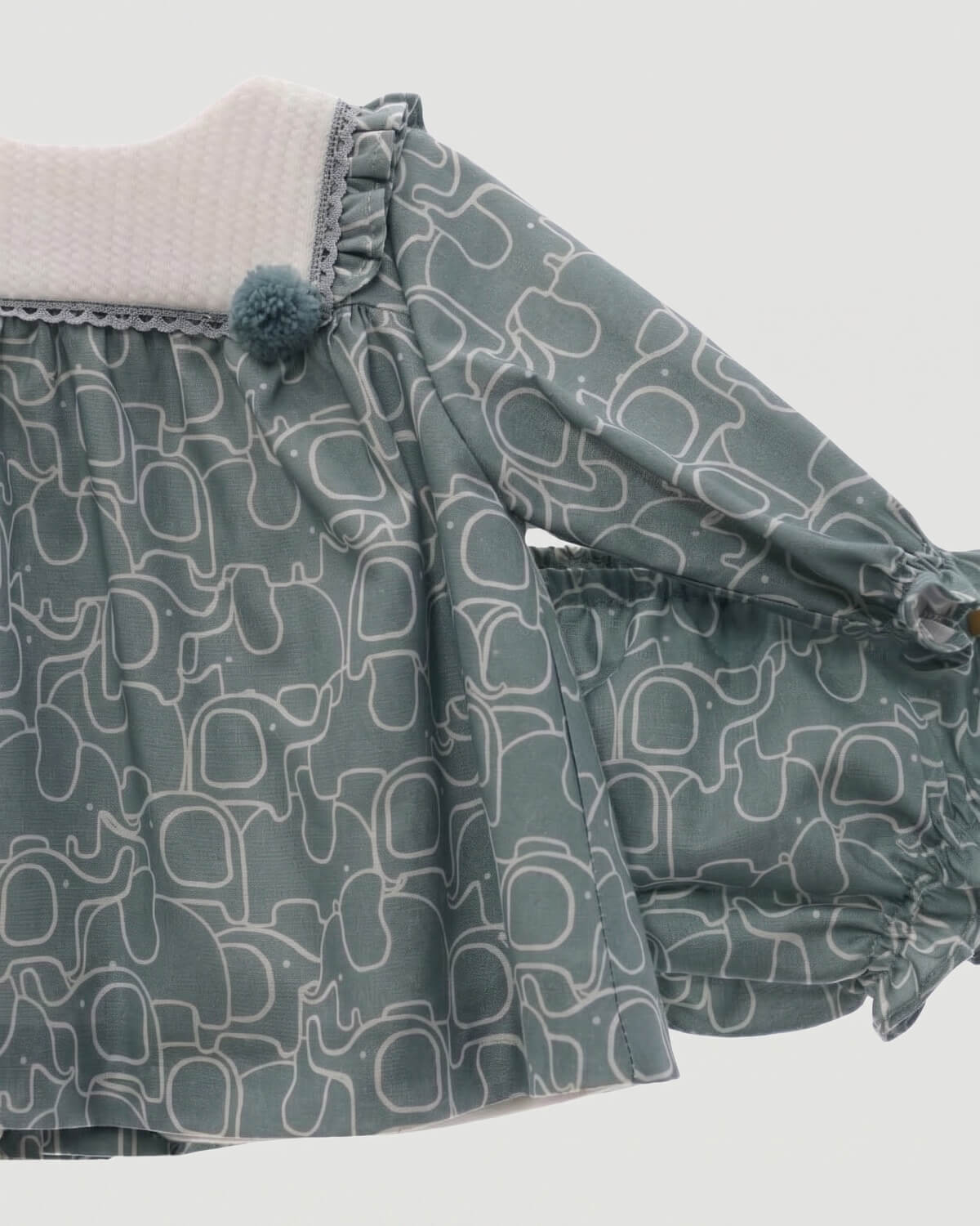 Close-up detail of textured bib collar, pom-pom trimming, and elephant print on traditional Spanish baby dress.