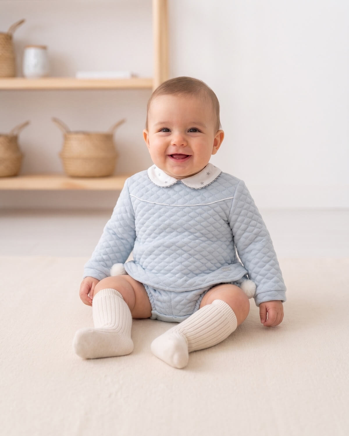 Baby boy wearing traditional Spanish blue quilted two-piece set with embroidered star collar and cream knee socks.